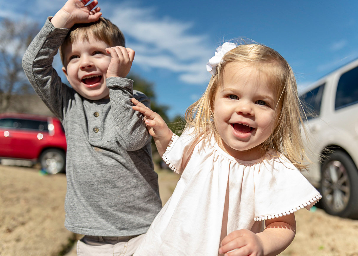 Young brother and sister running down the sidewalk and laughing together.