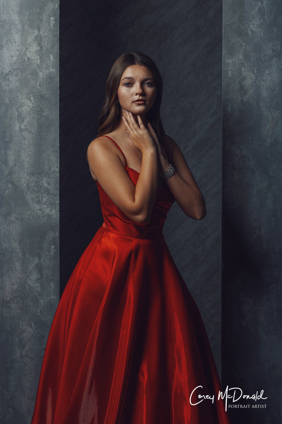 Woman in elegant red gown posing against a textured, dark background.