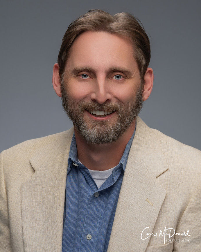 Man with beard and light brown hair wearing a beige jacket and blue shirt, smiling against a gray background.