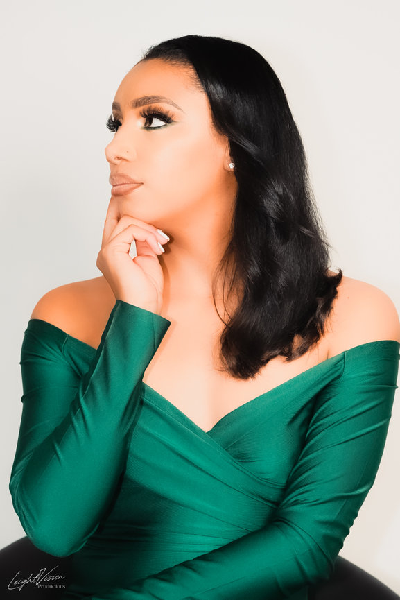 A woman wearing a green dress poses with her hand on her chin, reflecting a moment of deep thought.