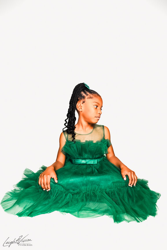 A young girl in a green dress sits on the floor, capturing a serene and delightful moment of childhood.