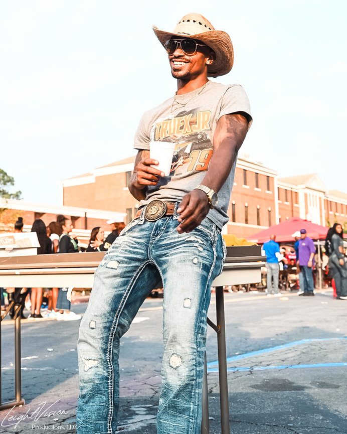 A smiling man wearing a cowboy hat and jeans, exuding a cheerful and relaxed demeanor.