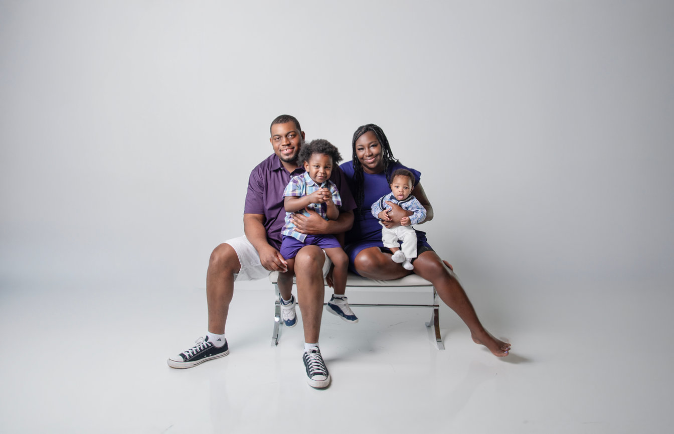 Family portrait with two adults and two young children sitting together against a neutral background.