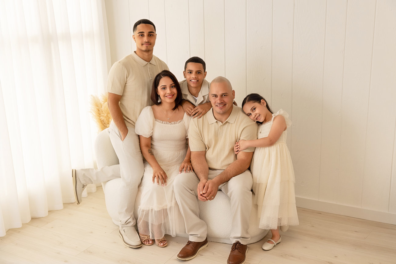 Family of five posed in a bright studio wearing coordinated cream clothing