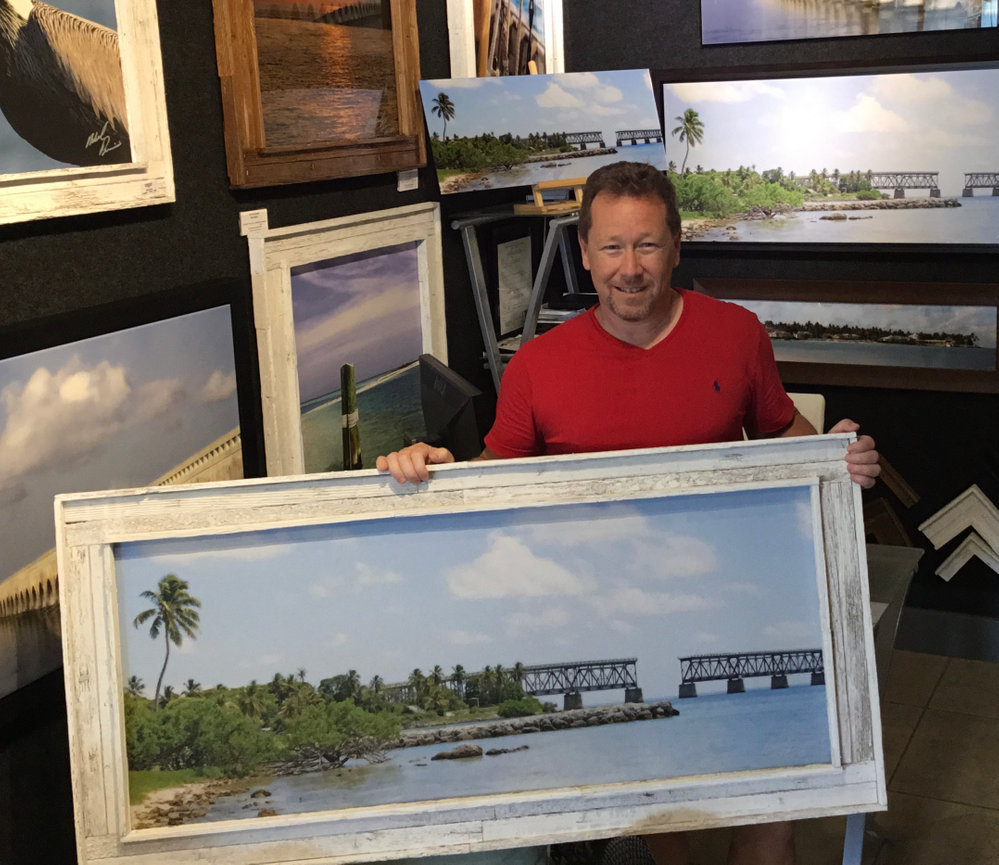 Photographer holding a framed beach landscape painting in a studio