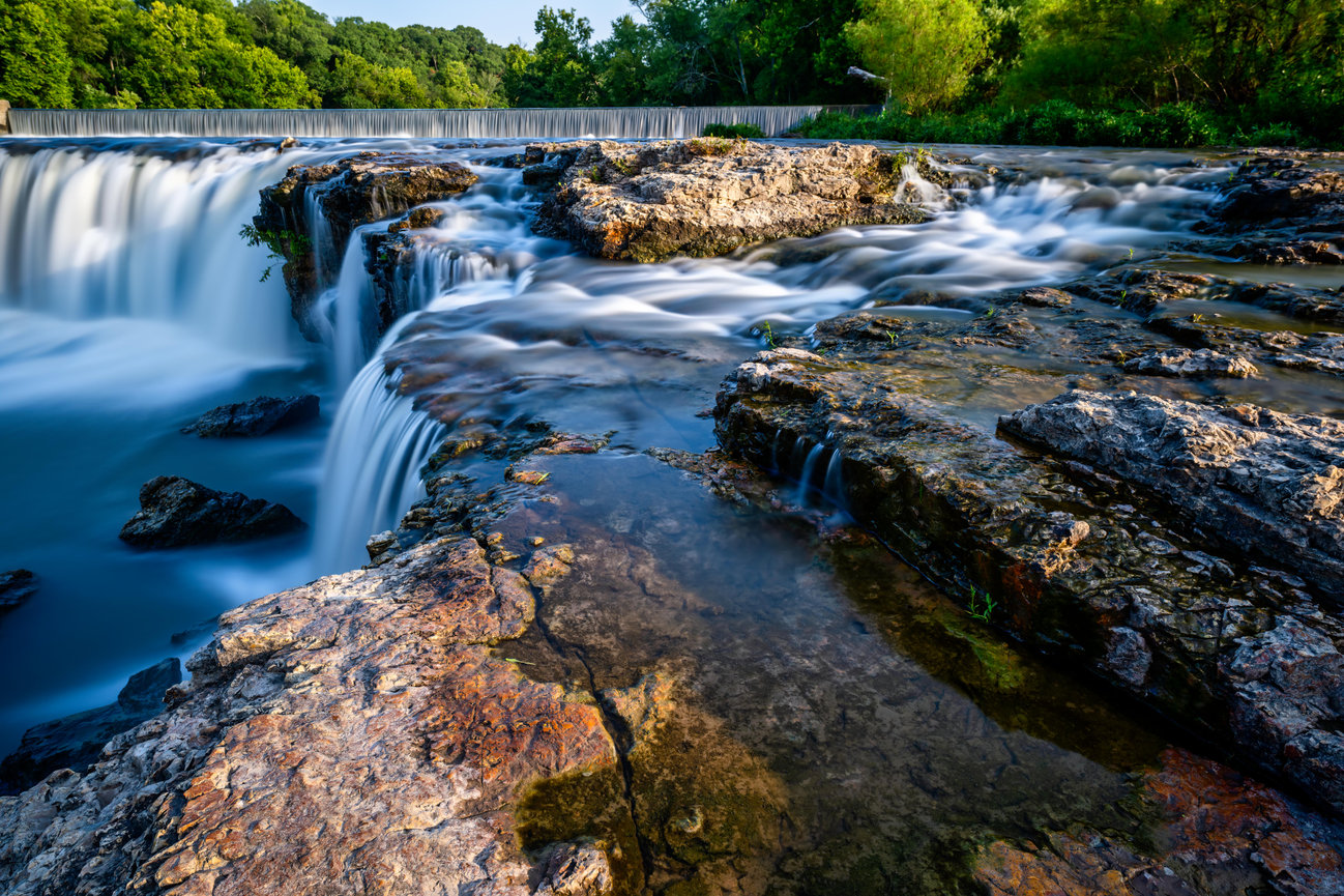 Long-exposure waterfall over rocky ledges in a lush green forest
