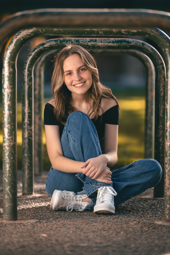 Senior year photo of girl sitting at a playground in jeans and tennis shoes at a park in Boise Idaho