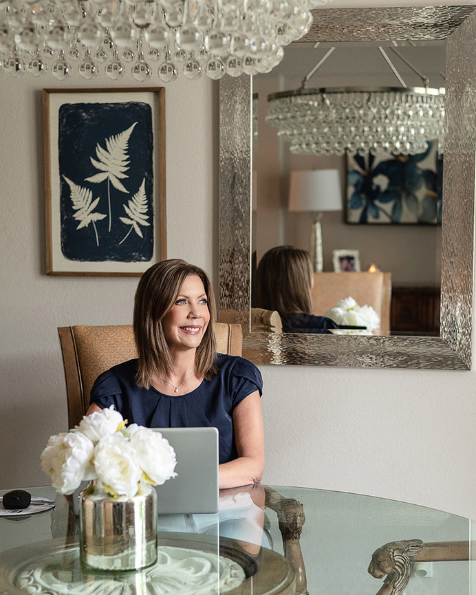 Female realtor in elegant setting, at the table with her computer, looking out the window and smiling, by Carlsbad Personal Branding Photographer, Stefanie Blue.