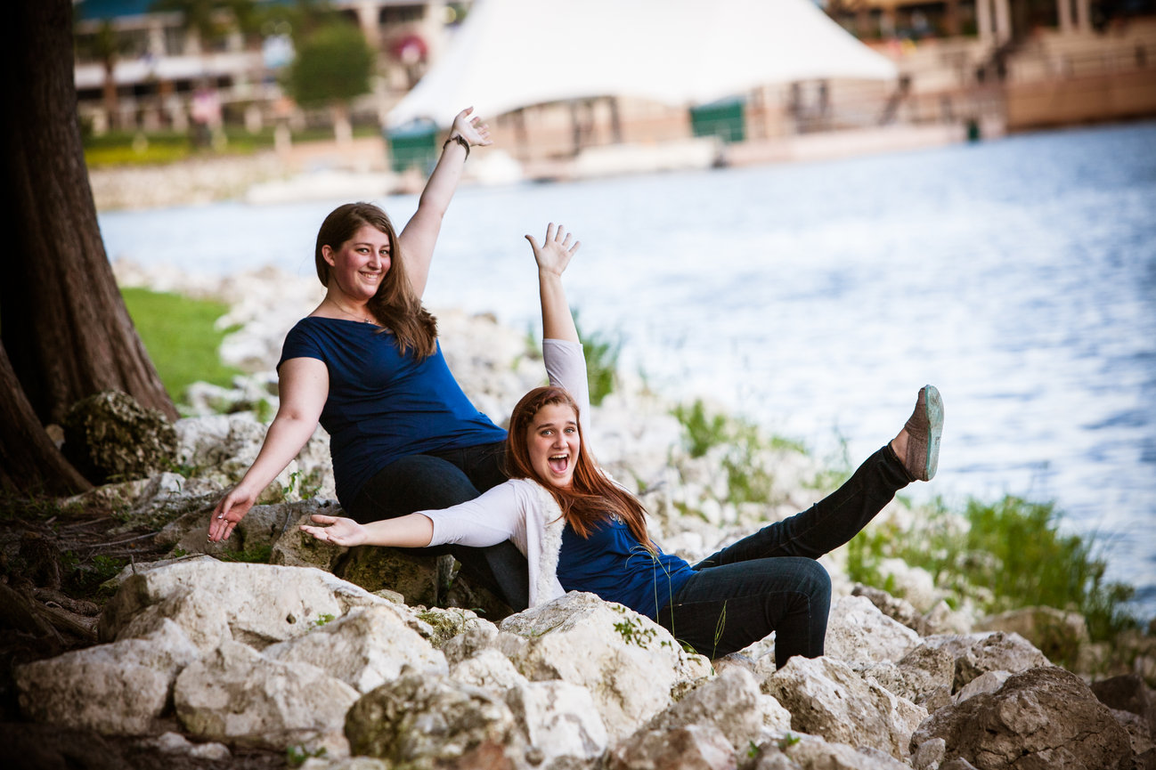 Two smiling women sitting on rocks by a lake