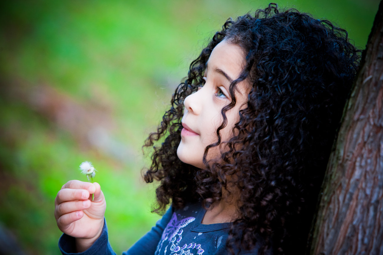Young girl holding a dandelion next to a tree