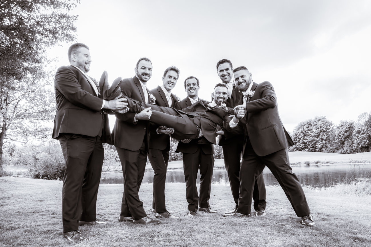 Groomsmen lifting the groom outdoors
