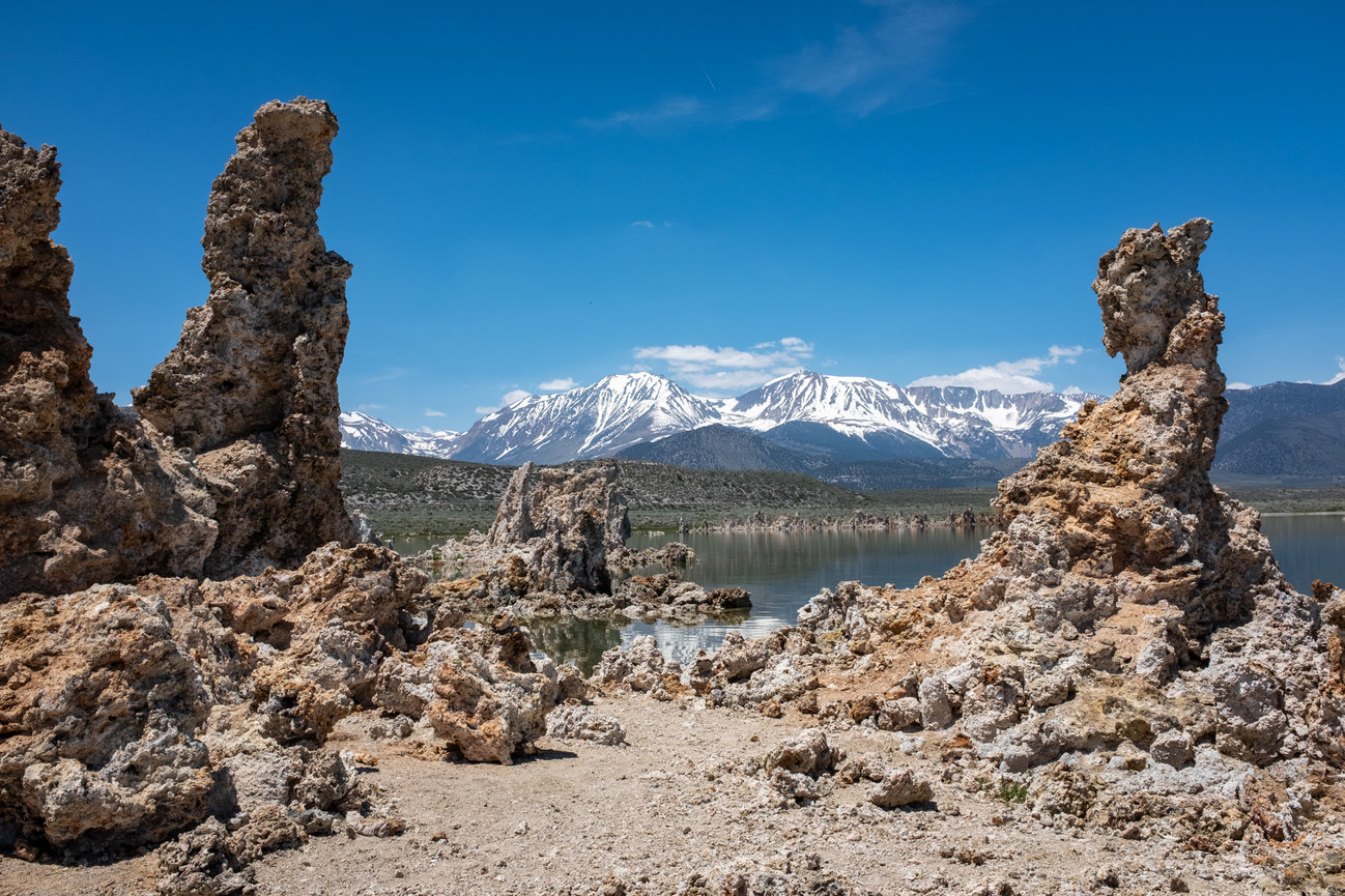 Jagged calcium tufa formations on the shoreline of Mono Lake with snow capped mountains in background.