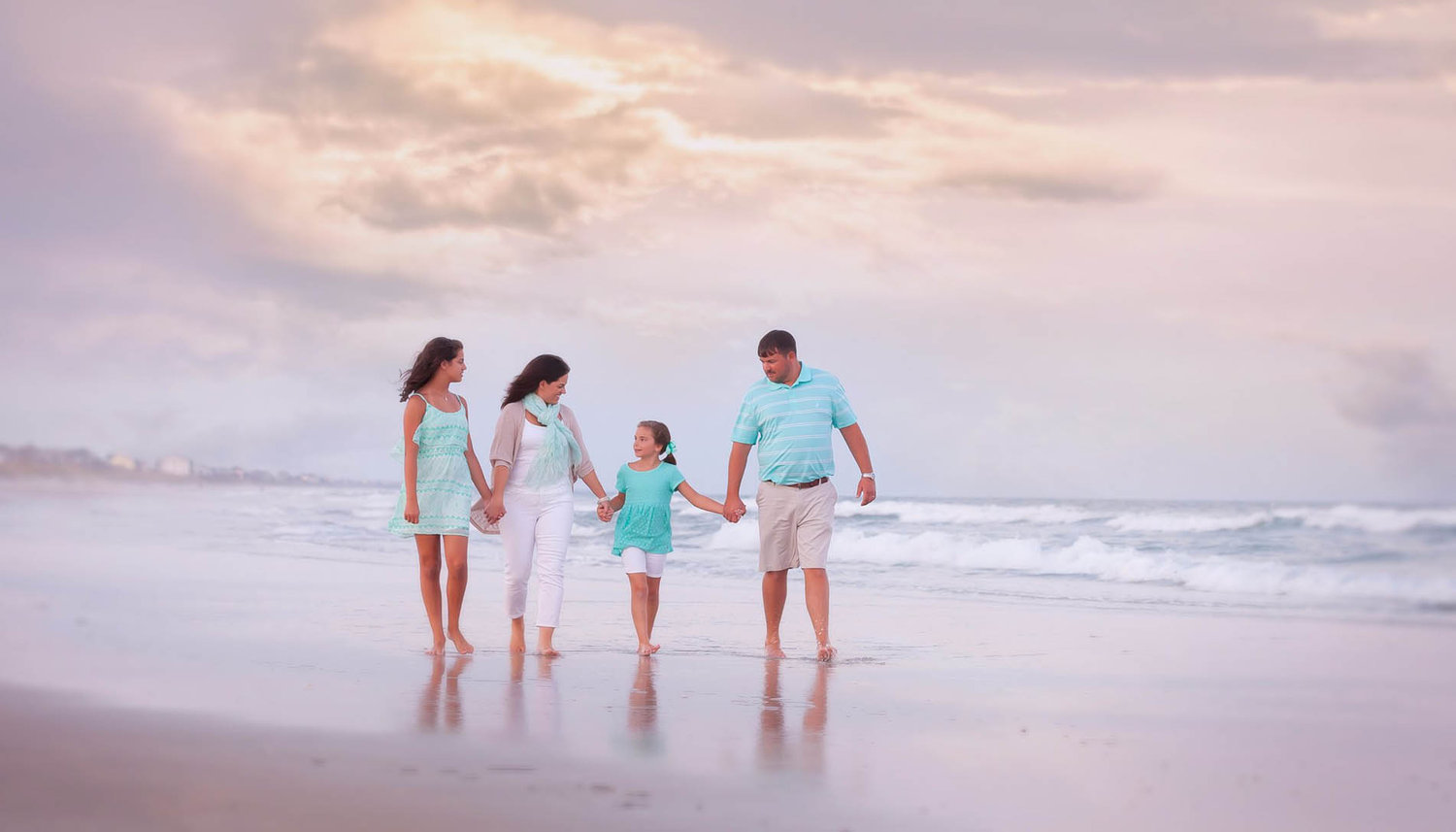 Family portrait at the beach during golden hour, with soft natural light and candid connection in a fine art style.