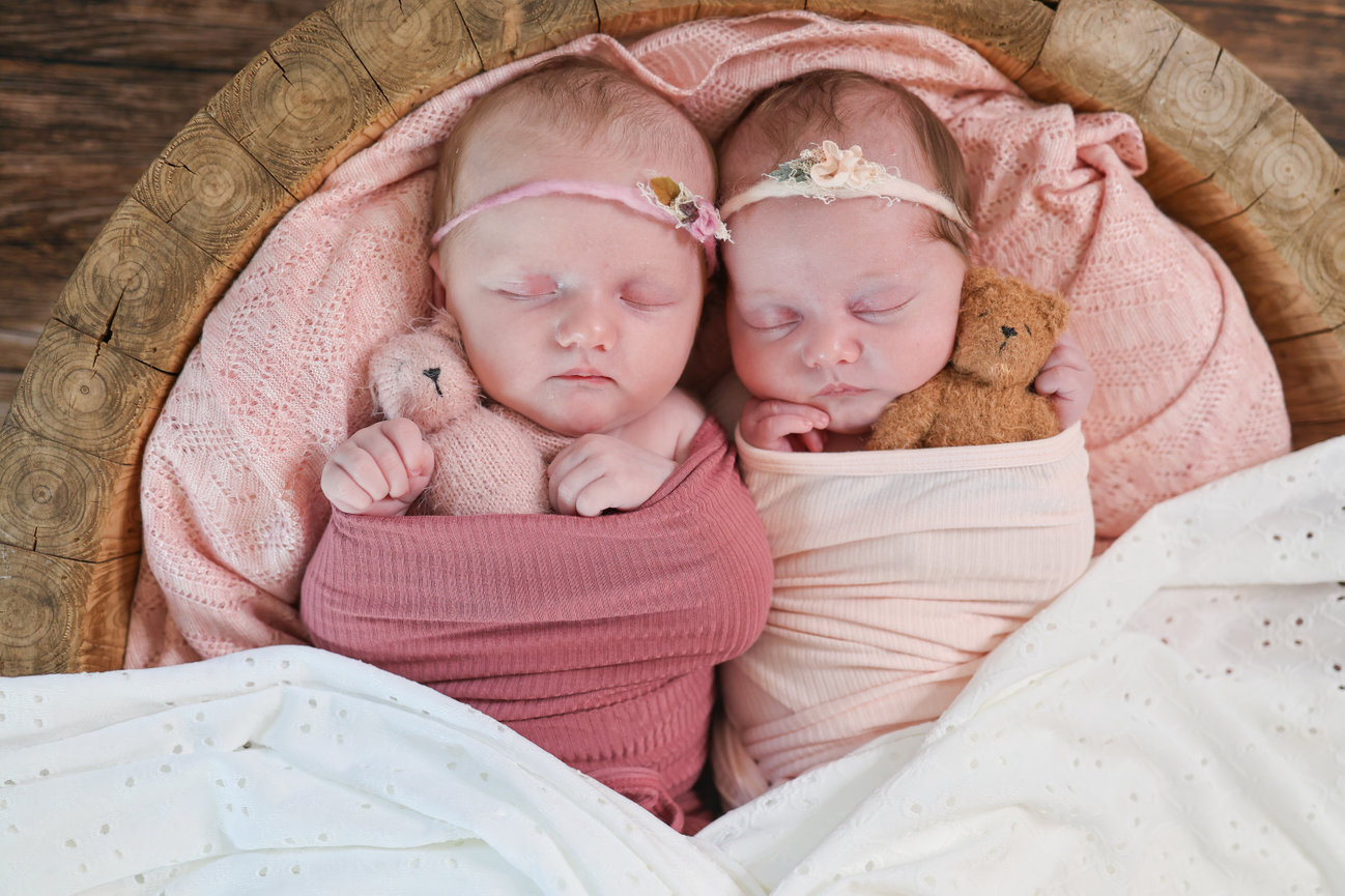 Twin newborn babies swaddled together in a basket
