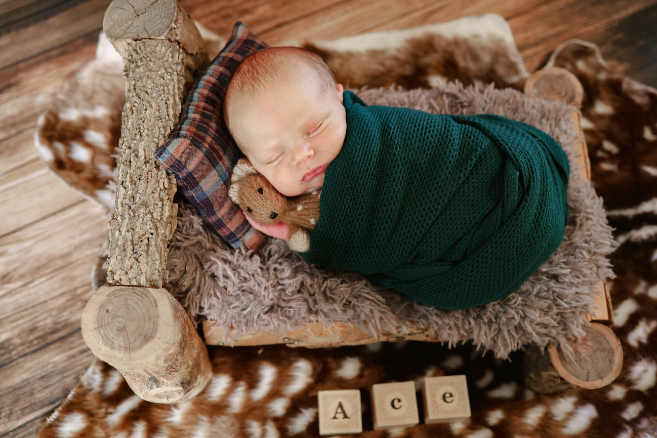 Sleeping newborn wrapped in dark green blanket in a rustic wagon