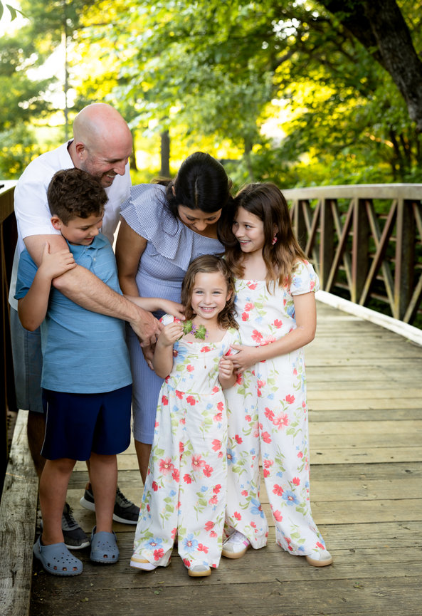 Happy family of five hugging on a wooden bridge in Veterans park