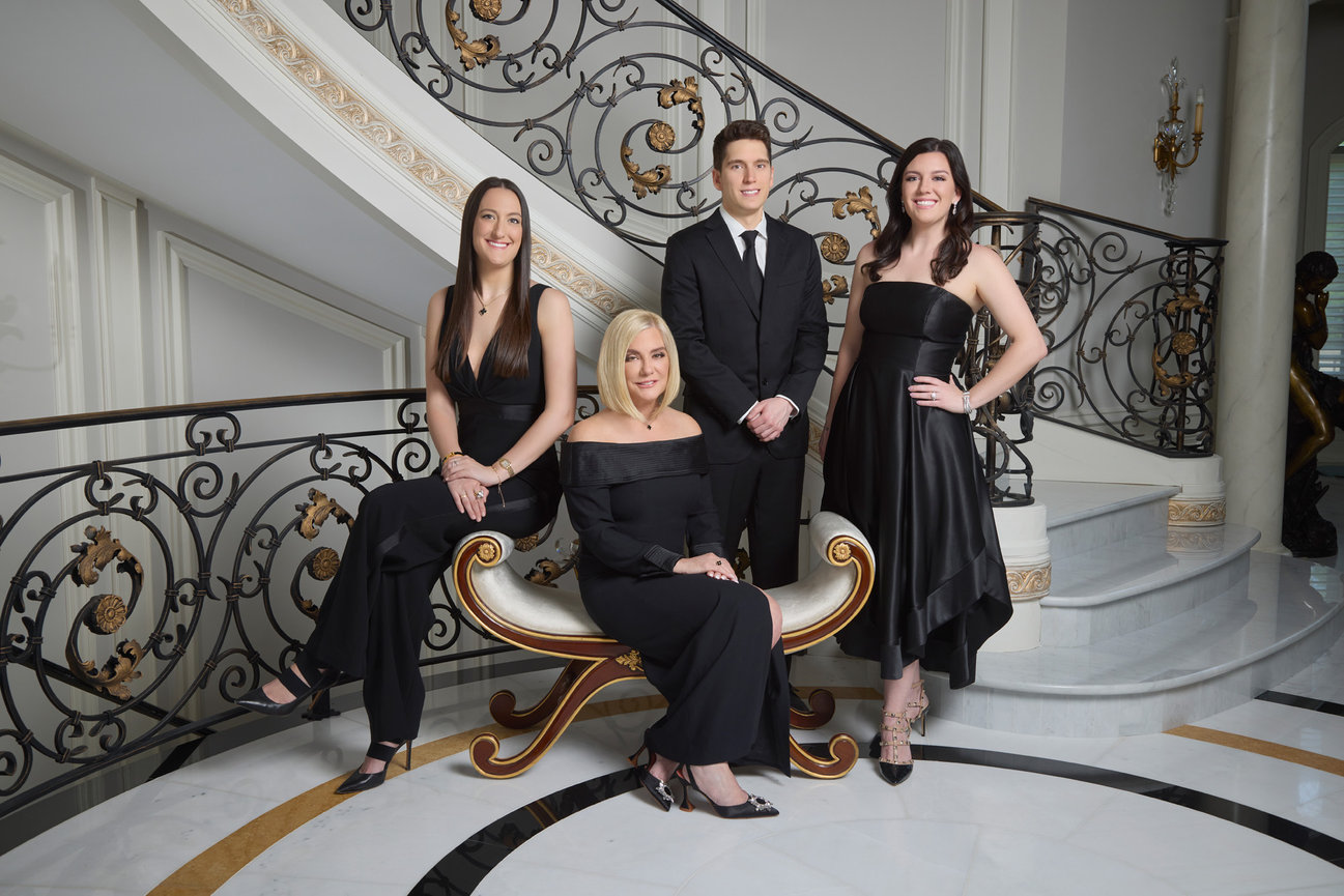 An in home portrait of an elegantyl dress mother and her three children in front of an ornately decorated marble staircase.