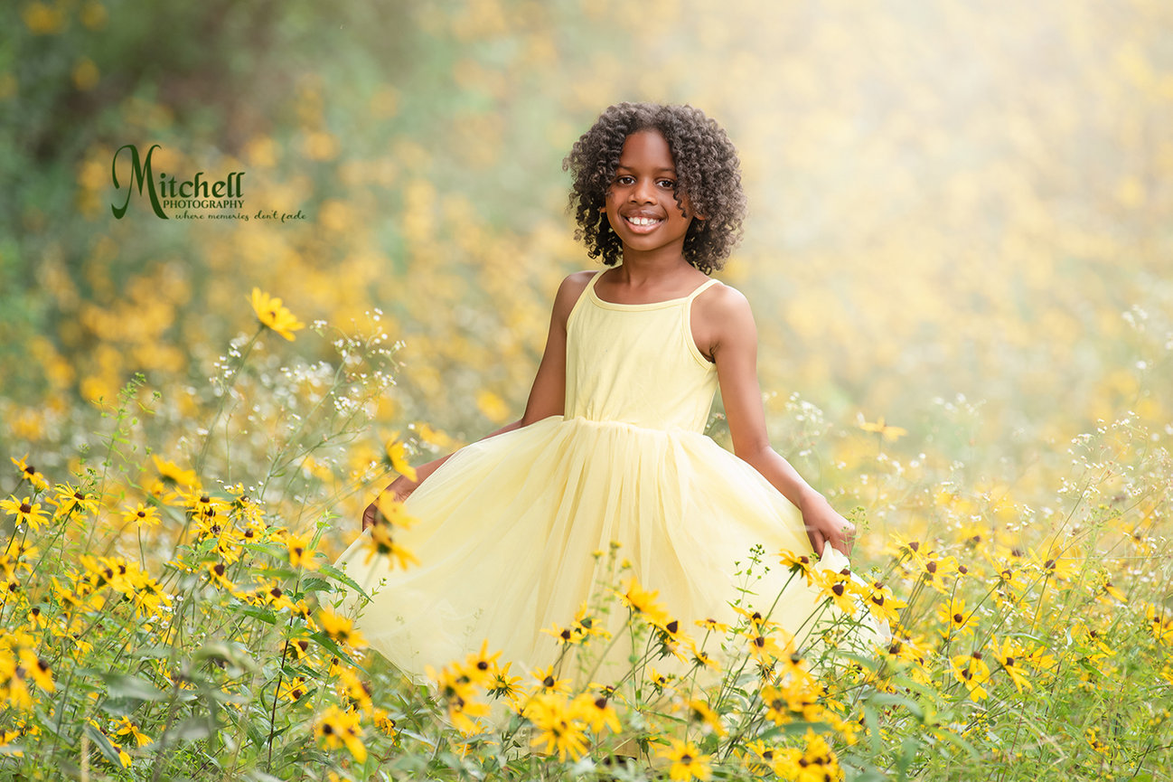 Smiling girl in a yellow dress standing in a field of yellow wildflowers