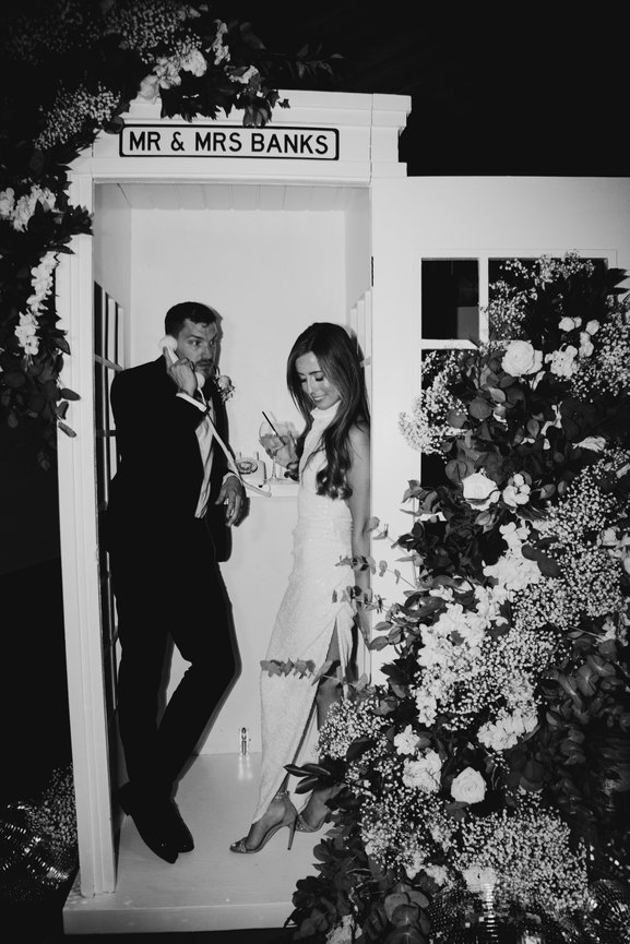 Cheshire editorial wedding photography at Owen House Wedding Barn. A couple posing in a floral-decorated phone booth, with a sign reading Mr & Mrs Banks, shot using flash.