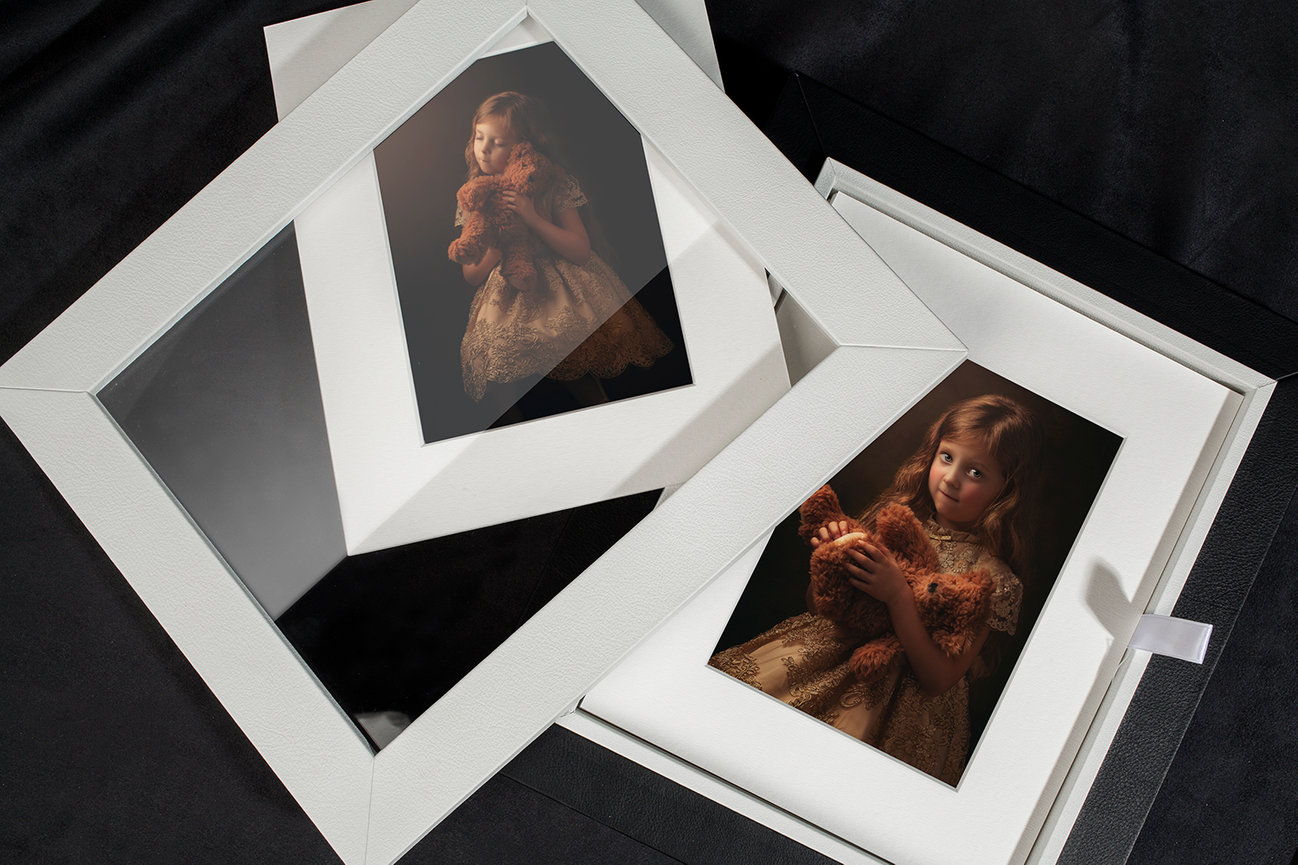 Framed portrait of a young girl with a teddy bear, displayed on a black surface.