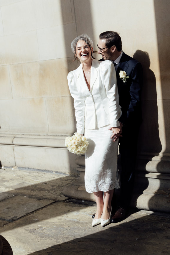 Editorial wedding photography of a bride and groom laughing together in bright sunlight, framed by the dramatic shadows of St George's Hall columns in Liverpool.