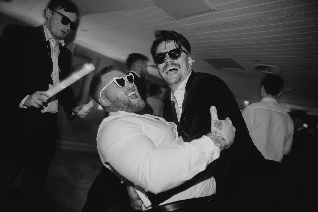 Direct flash editorial photography of a groom and guest in sunglasses on the dance floor at King Street Townhouse; a high-energy black and white party shot.