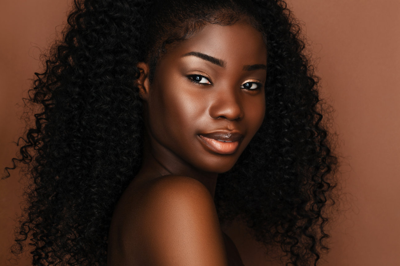 Studio portrait of a woman with natural curly hair and a warm background.