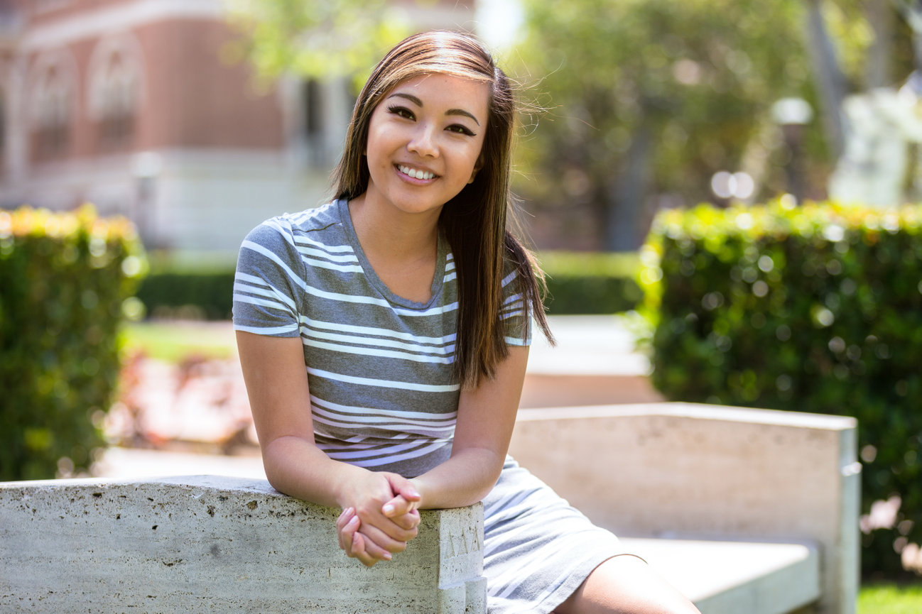 Smiling woman seated outdoors on a bench in a park-like setting.