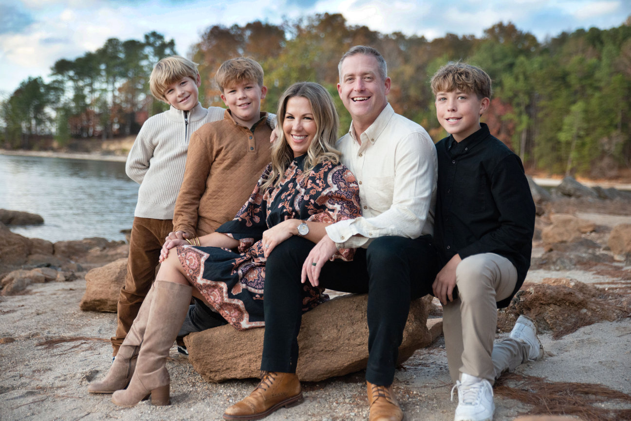 Family sitting together on rocks by the ocean at sunset.