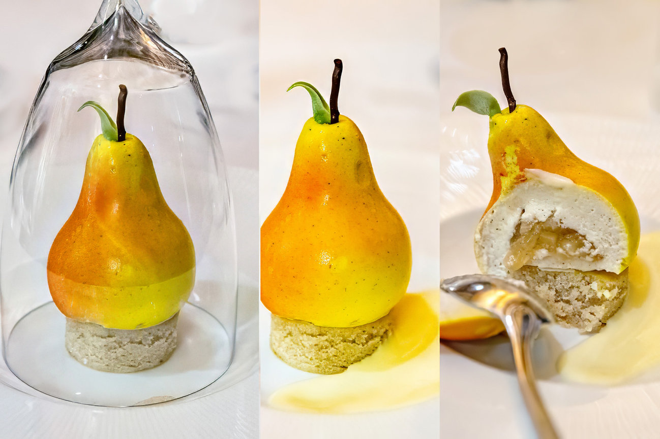 A pear-shaped dessert with a glossy finish, sitting on a cookie base, partially under a glass dome; one is partially eaten.