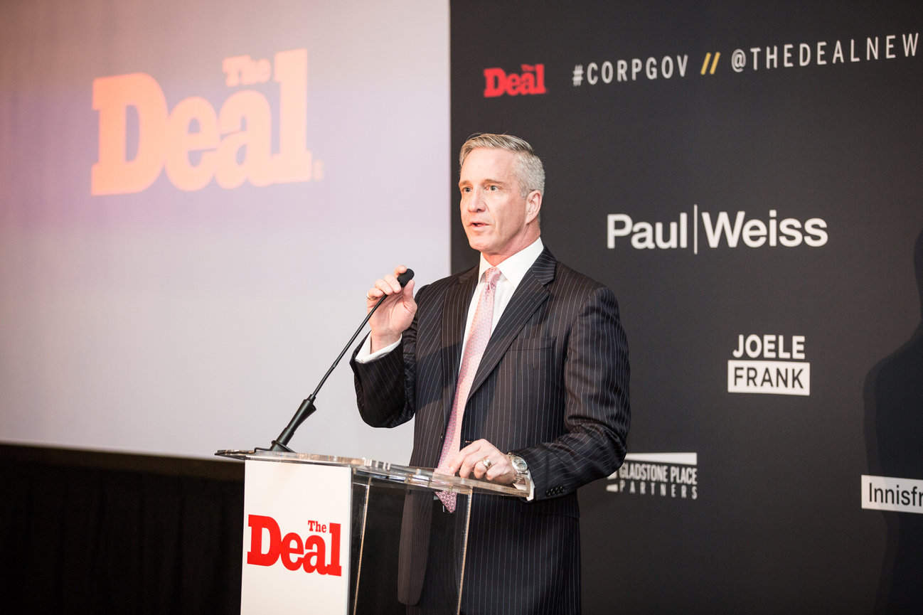 Man in a suit speaking at a podium during a The Deal event.