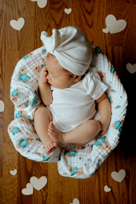 Newborn baby wrapped in a floral bucket on a wooden floor