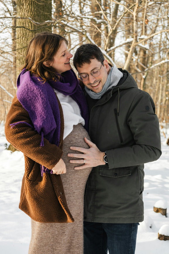 Pregnant couple standing together in a snowy forest