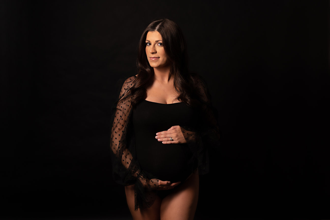 Confident and intimate studio maternity image with mother in curve-hugging bodysuit posed elegantly.