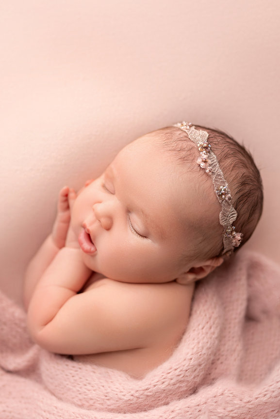 Newborn baby in soft neutral swaddle posed on solid blush pink backdrop in studio setting