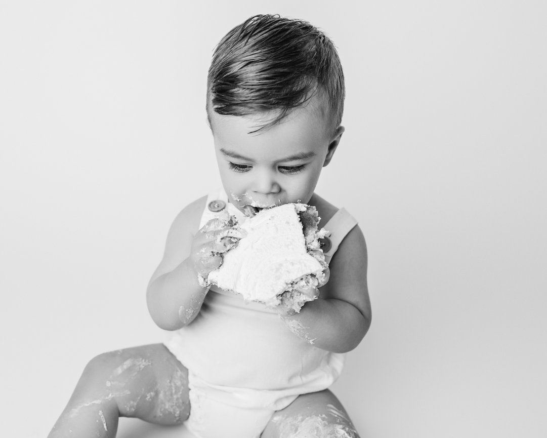Baby smashing cake with frosting on legs on white backdrop