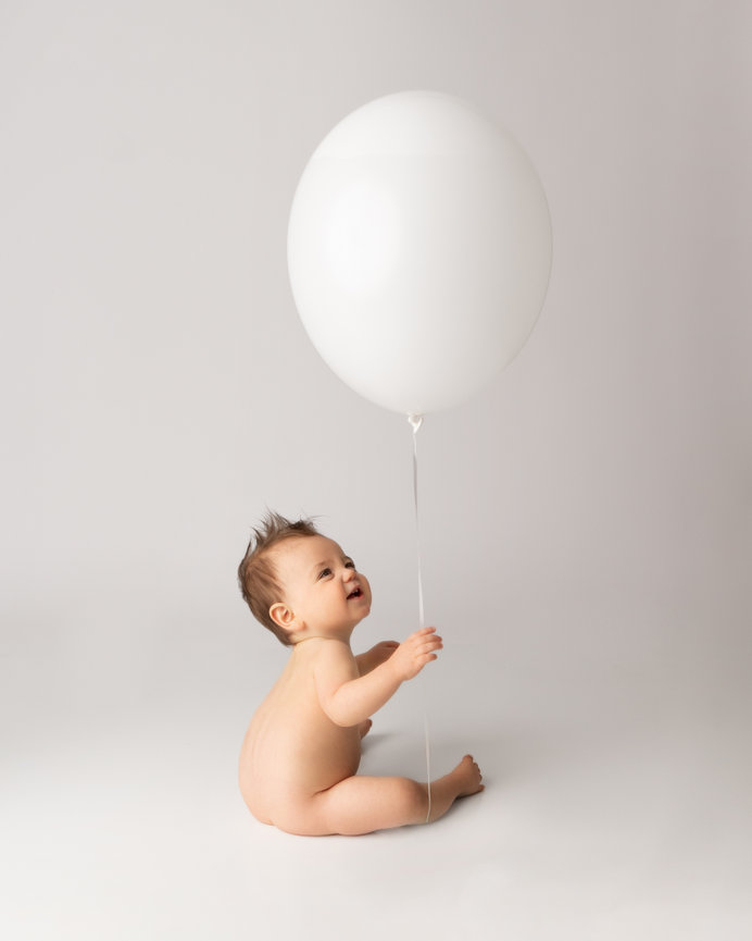 Naked baby reaching for floating balloon during first birthday session in Princeton