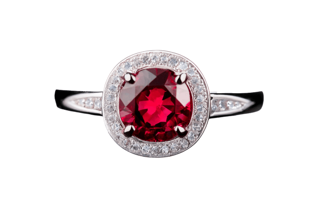 Elegant ring featuring a round-cut deep red ruby at the center, surrounded by a halo of small round diamonds, set in a polished white metal band with diamond accents along the shoulders, displayed on a white background