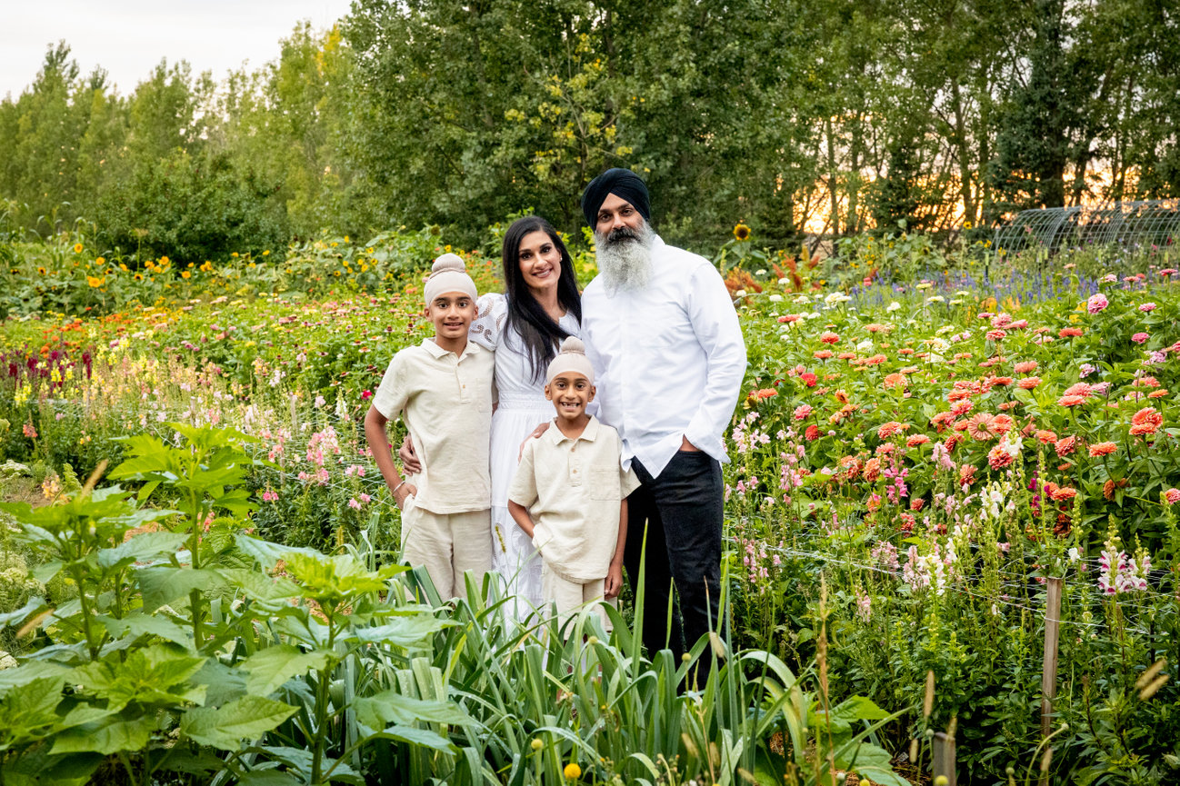 Family portrait in a vibrant garden with flowers, featuring a man, woman, and two boys.