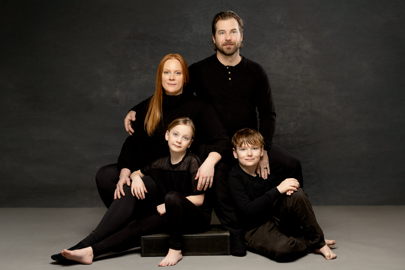 Family of four in black outfits posing against a dark backdrop.