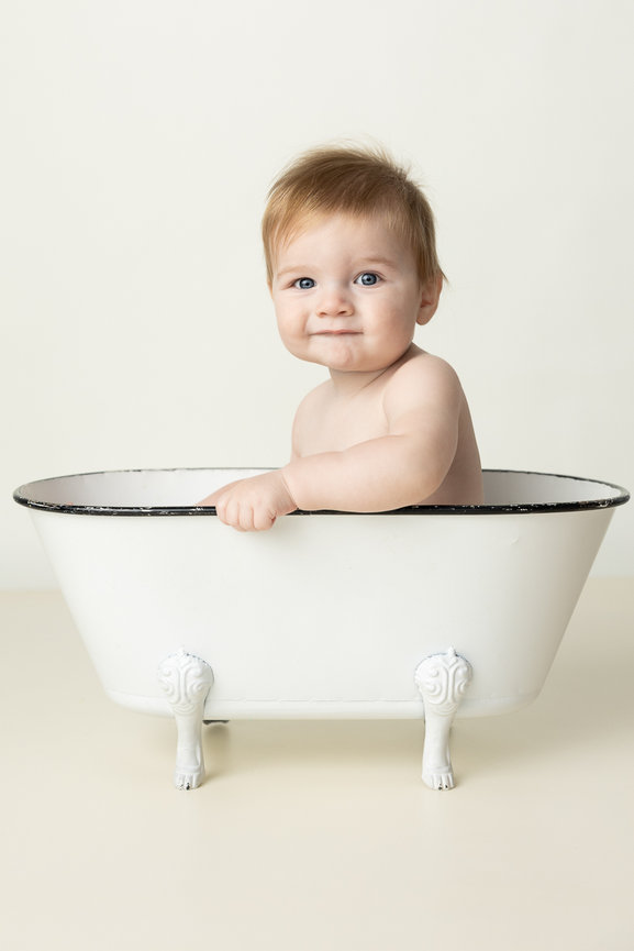 Baby sitting in a white vintage bathtub against a plain background at Winnipeg studio Sunny S-H Photography