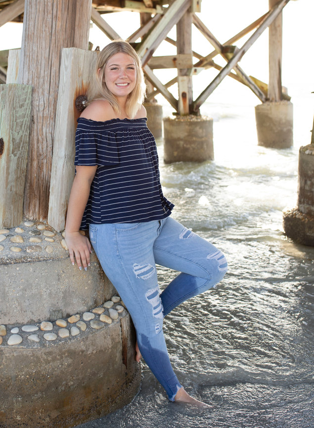 Beach Destination Senior Photo session of girl leaning against pier during her senior photoshoot with Angie Vincent of Heart to Art Photography.