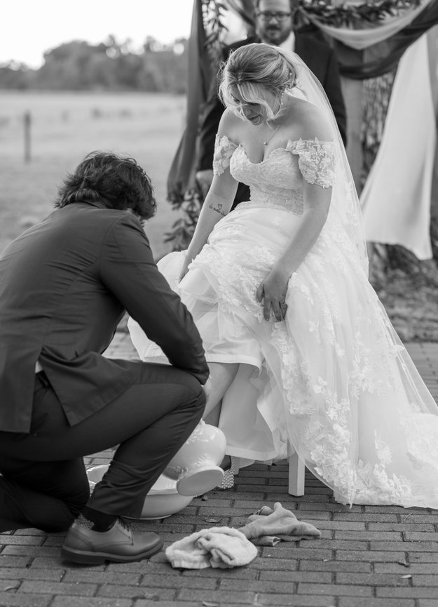 Photographer kneeling to adjust the bride's dress during a wedding portrait.