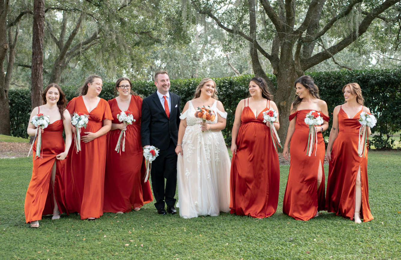 Wedding party posing together in red and cream attire outdoors.