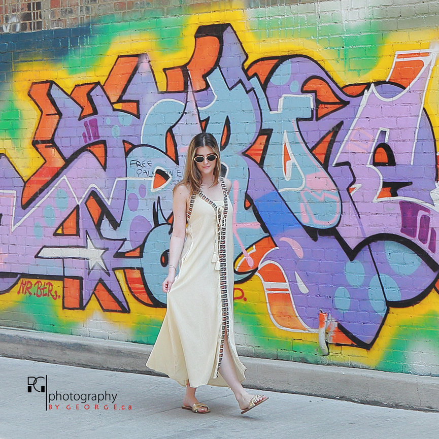 Model wearing a neutral bohemian dress in front of colorful street art, representing Summer 2026 fashion trends.
