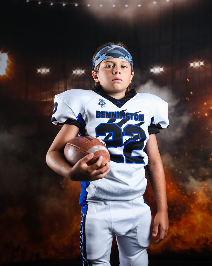 Young football player in full gear holding a football, with a dramatic stadium background.