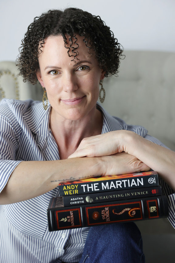 Woman holding a stack of books, including The Martian and a Haunting in Venice, in a cozy indoor portrait. headhshot photoshoot melbourne