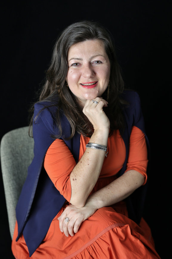 Smiling woman in orange dress and navy shawl posing in a studio portrait against a black background. headhshot photoshoot melbourne