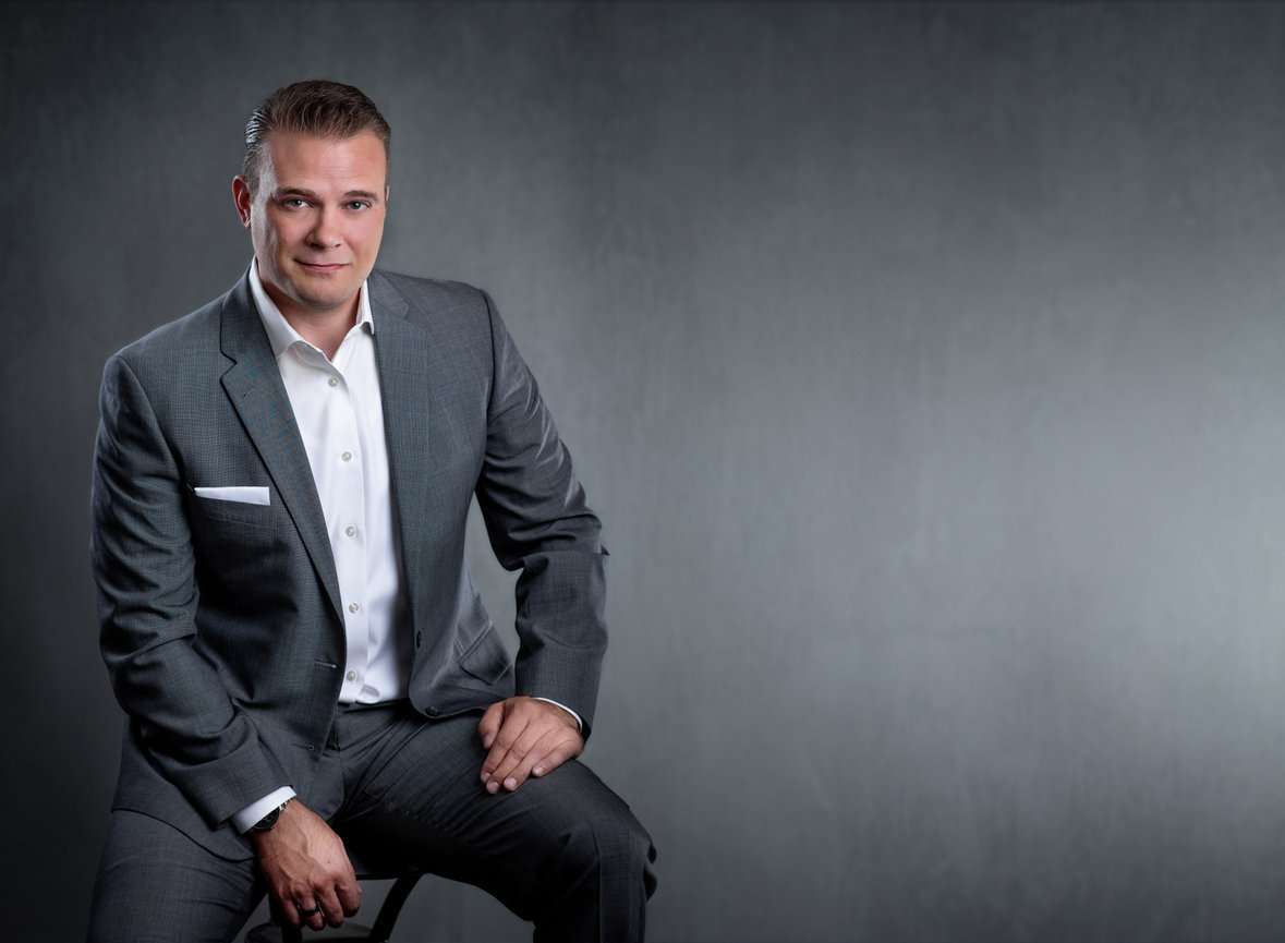 Business professional in a gray suit sitting against a textured gray background.