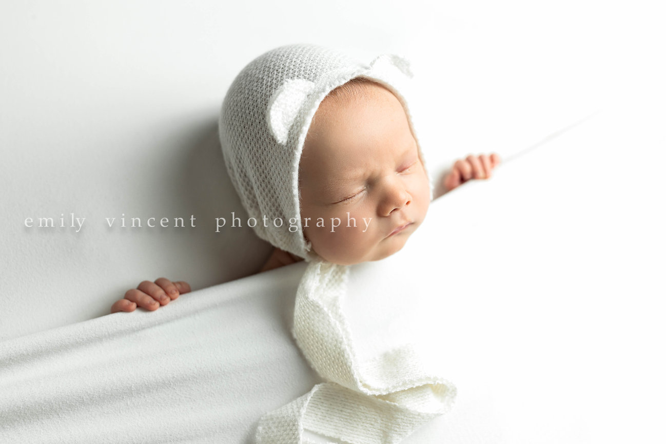 Newborn baby with white bear hat under white blanket in newborn photo session